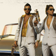 Two soldiers wearing cream linen suits and standing in front of a bronze convertible in Far Cry 6.